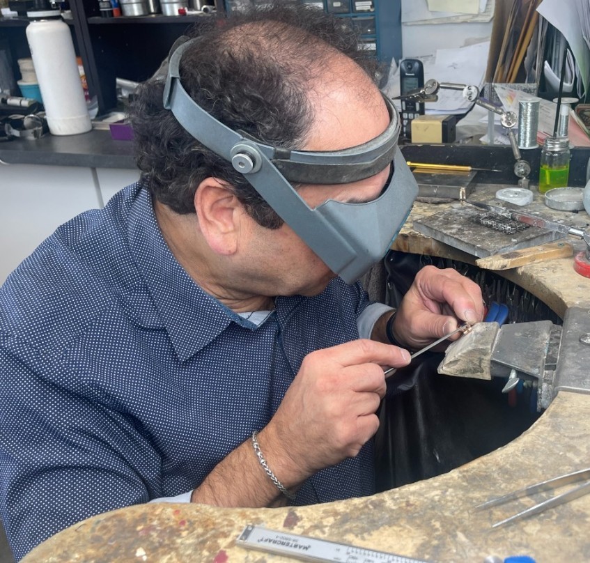 Goldsmith crafting and polishing a custom cufflink piece at a workshop bench