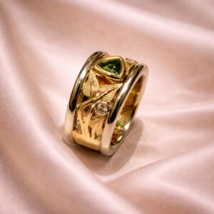 Gold gemstone ring with a triangular green stone, textured design, and diamond accent