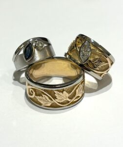 Custom two-tone gold and silver rings with engraved leaf designs and gemstone accents